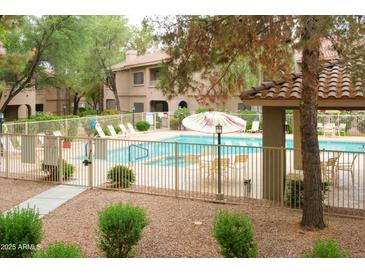 Community pool area with lounge chairs and tables, surrounded by mature landscaping and a wrought iron fence at 15252 N 100Th St # 1172, Scottsdale, AZ 85260