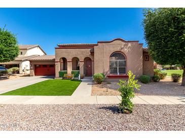Charming single-story home with synthetic grass, mature trees, and a red garage door at 15416 W Valentine St, Surprise, AZ 85379