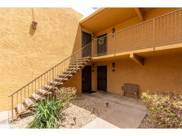 Tan building with stairs leading up to second floor condos and small patio with a bench for residents at 8500 E Indian School Rd # 233, Scottsdale, AZ 85251