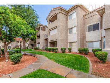 Charming condo building featuring manicured lawn, lush landscaping, and a tiled roof under a clear blue sky at 3830 E Lakewood Pkwy # 3099, Phoenix, AZ 85048