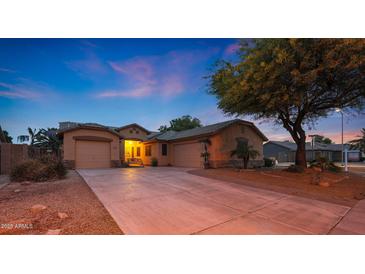 Charming home featuring three-car garage and inviting curb appeal with a mature shade tree at dusk at 15245 W Crocus Dr, Surprise, AZ 85379