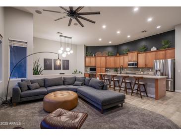 Open-concept living room featuring a gray sectional couch, modern lighting, and a kitchen with stainless steel appliances at 8544 W Mary Ann Dr, Peoria, AZ 85382