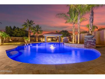 Stunning backyard pool with water feature, cabana, and lush tropical landscaping perfect for entertaining at 1179 E Regent Dr, Gilbert, AZ 85298
