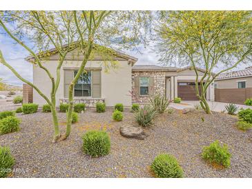 Charming home exterior featuring desert landscaping with stone accents and mature trees at 18624 W Cathedral Rock Dr, Goodyear, AZ 85338