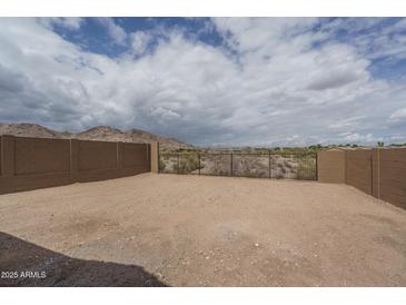 Desert backyard featuring a brick wall and metal gate with mountain views under a partly cloudy sky at 2823 N 212Th Dr, Buckeye, AZ 85396
