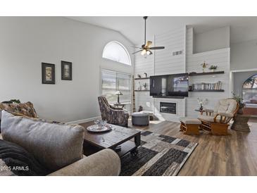 Bright living room featuring wood floors, a ceiling fan, and a fireplace with a shiplap accent wall at 10733 W Clover Way, Avondale, AZ 85392