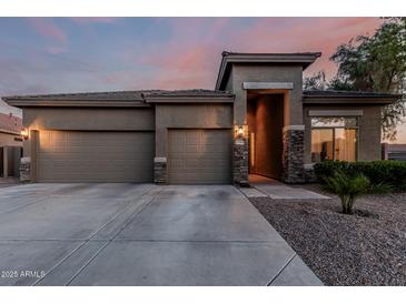 Charming exterior view showcasing a three-car garage and desert landscaping at dusk at 22166 N Lakeside Dr, Maricopa, AZ 85138