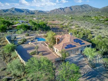 Stunning aerial view of a desert home, featuring a pool, tile roof, and solar panels against a mountain backdrop at 6524 E Rockaway Hills Dr, Cave Creek, AZ 85331