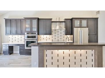 This kitchen features dark cabinets, stainless steel appliances, and a tile backsplash for a modern design at 7272 E Gainey Ranch Rd # 117, Scottsdale, AZ 85258