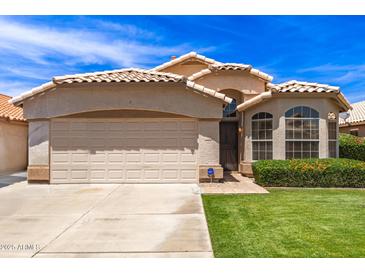 Charming single-story home with a tile roof, manicured lawn, and a two-car garage on a sunny day at 7930 W Wescott Dr, Glendale, AZ 85308
