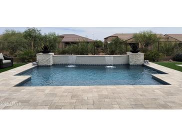 Backyard swimming pool featuring a tiled waterfall feature and travertine tile decking at 24035 N 171St Dr, Surprise, AZ 85387