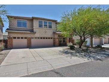 Two-story home featuring a three-car garage, desert landscaping, and a mature shade tree in the front yard at 30263 W Crittenden Ln, Buckeye, AZ 85396