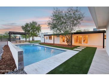 A backyard featuring a sparkling pool, turf grass, and a covered patio area, perfect for relaxation at 3043 E Hartford Ave, Phoenix, AZ 85032