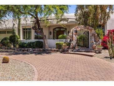 Front exterior of home with brick driveway, stone entry, and lush landscaping at 11717 E Estrella Ave, Scottsdale, AZ 85259