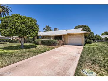 Charming single-story home featuring a well-manicured lawn, a two-car garage, and mature trees on a sunny day at 13631 N 103Rd Ave, Sun City, AZ 85351