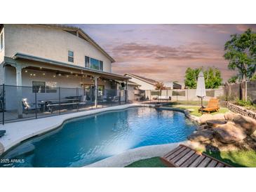 Inviting backyard pool with rock features, a safety fence, patio, and lovely landscaping at 7931 W Harmony Ln, Peoria, AZ 85382