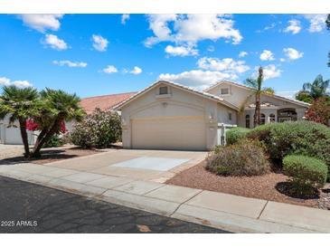 Charming single-story home with a two-car garage, mature landscaping, and a tile roof, set against a beautiful blue sky at 21675 N 61St Ave, Glendale, AZ 85308