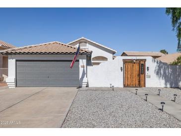 Charming home featuring a gray garage door, a wooden gate, and desert landscaping at 13320 N 82Nd Dr, Peoria, AZ 85381