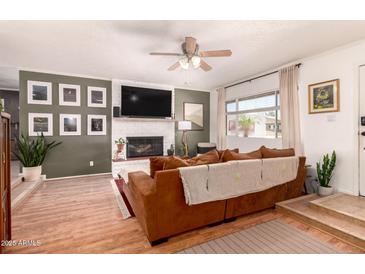Inviting living room features a white brick fireplace, TV, fan, neutral walls, and a cozy, comfortable brown sofa at 5031 W Grandview Rd, Glendale, AZ 85306