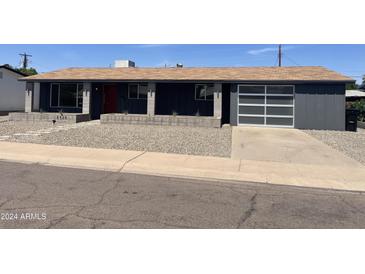 Charming single-story home with a modern grey exterior, stone landscaping, and a transparent glass garage door at 8520 E Mackenzie Dr, Scottsdale, AZ 85251