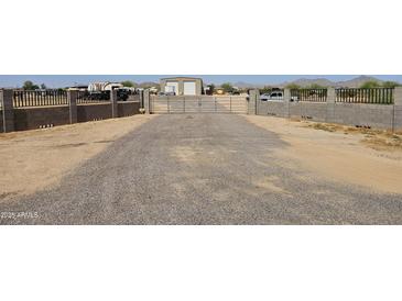 Gravel driveway leading to a gated property with metal buildings, enclosed by concrete fencing with wrought iron toppers at 30940 N Varnum Rd, San Tan Valley, AZ 85143