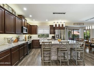 Well-lit kitchen featuring wood floors, cabinets, stainless appliances, and island with bar seating at 16202 N 61St Ave, Glendale, AZ 85306