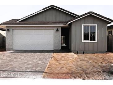 Charming single-story home with gray siding, brick driveway, a white garage door, and well-manicured landscaping at 18165 W Larkspur Dr, Goodyear, AZ 85338