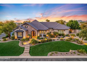 A stunning single-Gathering home has lush green landscaping, a stone facade, and a welcoming entrance at sunset at 6918 E Ivyglen St, Mesa, AZ 85207