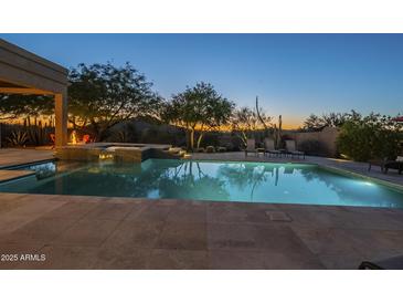 Beautifully lit backyard pool area with a spa, lounge chairs, and lush desert landscaping at dusk at 8248 E Arroyo Hondo Rd, Scottsdale, AZ 85266