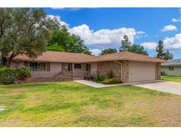 Charming single-story home featuring a brick facade, lush lawn, and well-manicured landscaping at 9805 W Gulf Hills Dr, Sun City, AZ 85351