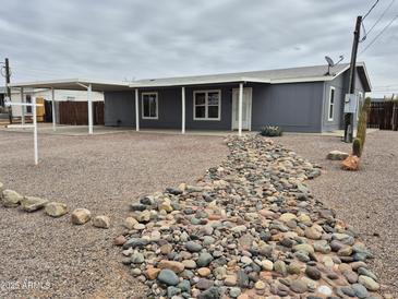 Charming single-story home with a covered carport, grey siding, and a decorative rock garden at 329 N 83Rd Pl, Mesa, AZ 85207