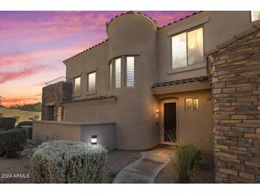 Inviting home exterior featuring a stone accent wall, desert landscaping, and soft illumination at dusk at 19475 N Grayhawk Dr # 1115, Scottsdale, AZ 85255