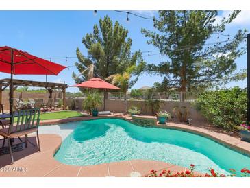 Inviting backyard oasis features a sparkling pool, lush landscaping, and cozy pergola with string lights at 17541 W Statler Dr, Surprise, AZ 85388