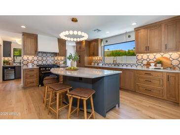 Modern kitchen featuring wood cabinets, geometric backsplash, black appliances, and an island with seating at 7328 E Laredo Ln, Scottsdale, AZ 85250