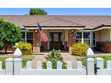 Charming home entrance with brick accents, American flag, mature landscaping, and white picket fence at 3160 E Fox St, Mesa, AZ 85213