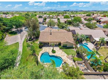 Aerial view of a home with a kidney-shaped pool, stone patio, and lush landscaping in a golf course community at 7734 E Monica Dr, Scottsdale, AZ 85255