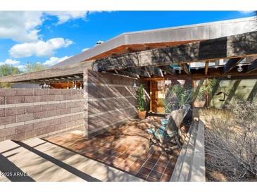 Open front porch with a brick floor, wood beams, potted cacti, and two chairs, creating an inviting entrance at 25232 N Horseshoe Trl, Scottsdale, AZ 85255