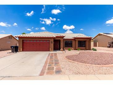 Charming single-story home featuring a red garage door, beautiful desert landscaping, and a white tiled roof at 6302 E Portia St, Mesa, AZ 85215