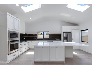 Bright, open kitchen features an expansive island, stainless steel appliances, skylights, and modern black backsplash at 4246 E Mulberry Dr, Phoenix, AZ 85018