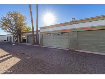 View of well-maintained garages with neutral paint and mature trees under a blue sky at 7132 N 63Rd Dr, Glendale, AZ 85301
