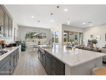 Open concept kitchen features an island, granite countertops, gray cabinetry, and is connected to the dining and living area at 21134 W Minnezona Ave, Buckeye, AZ 85396