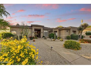 Inviting single-story home with desert landscaping, paver walkway, and a cozy covered porch, accentuated by a colorful sunset at 9534 E Monument Dr, Scottsdale, AZ 85262