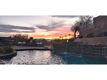 Inviting pool area with a stone waterfall feature and built-in seating, set against a vibrant sunset backdrop at 136 E Desert Wind Dr, Phoenix, AZ 85048
