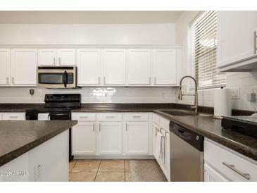 Bright kitchen features white cabinets, black appliances, and dark countertops at 17613 N 114Th Ln, Surprise, AZ 85378