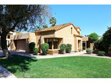 Tan single-story home with tile roof, manicured lawn, mature trees, and a two car garage at 9115 N 101St Way, Scottsdale, AZ 85258