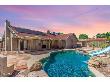 Backyard pool with a slide and stone features is surrounded by a fence and has a covered patio area for relaxing at 15825 N 45Th St, Phoenix, AZ 85032