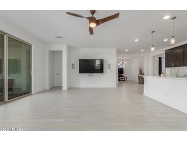 Spacious living room featuring white tile flooring, a modern ceiling fan, and a wall-mounted television for entertainment at 25601 N 140Th Ln, Surprise, AZ 85387