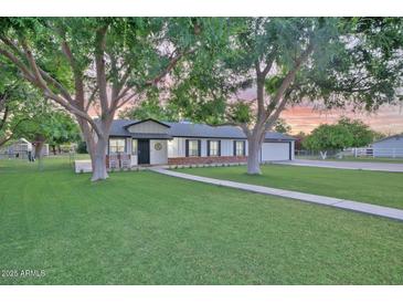 Charming single-story home featuring a lush green lawn, mature shade trees, and a welcoming front porch with rocking chairs at 1886 S 141St Pl, Gilbert, AZ 85295