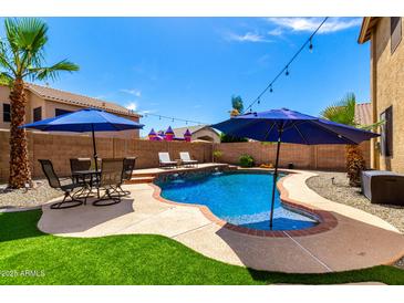 Beautiful backyard pool featuring a rock waterfall, lounge chairs, outdoor seating, and a lush green lawn at 16565 W Garfield St, Goodyear, AZ 85338