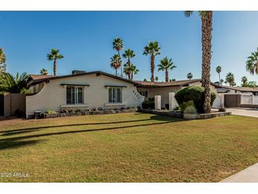 Charming single-story home featuring a well-manicured lawn, desert landscaping, and numerous stately palm trees at 5333 E Sheena Dr, Scottsdale, AZ 85254